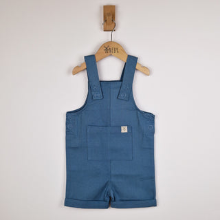 Flat lay of slate blue kids' cotton dungaree shorts, front view. The organic cotton fabric is soft and breathable, with a simple and timeless design.