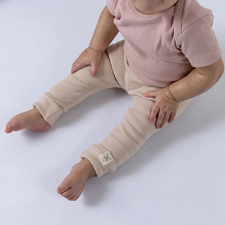 A baby wearing oat-coloured organic leggings with a matching ribbed pink top. The Aneby hem tag is visible on the leggings, highlighting the brand’s attention to detail. The baby’s legs are in focus, showing the soft, stretchy fabric designed for comfort and movement.