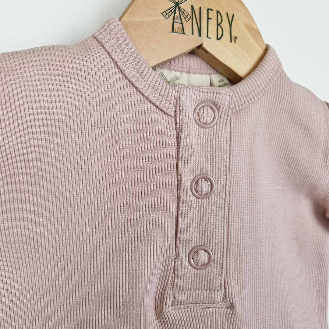 Dusty pink short sleeve rib baby romper on wooden hanger, close up front view of the front placket opening with 3 pink metal poppers and the neckline neatly finished with chunky rib binding.