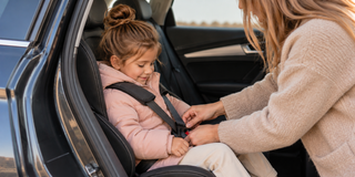 Parent securing a young child in a car seat, illustrating winter car seat safety and the importance of removing bulky coats before travelling.