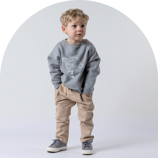 Boy stood with hands in pockets wearing beige chino style trousers and grey jumper with astronaut print