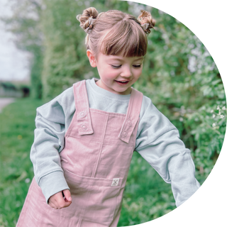 Girl in garden picking flowers wearing pink dungaree dress and green jumper