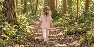Toddler wearing an Aneby pink windmill T-shirt and cream leggings on a woodland walk