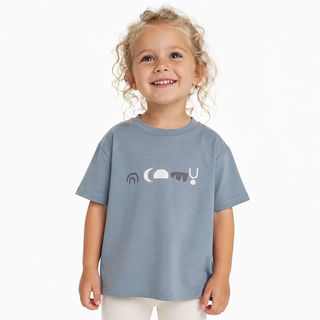 A young girl with curly blonde hair smiling, wearing a grey/blue t-shirt with a minimalist graphic across the chest, set against a plain white background.