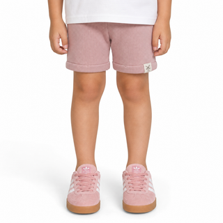 A child wearing dusty pink shorts with rolled cuffs and matching pink trainers, shown from the waist down on a white background.