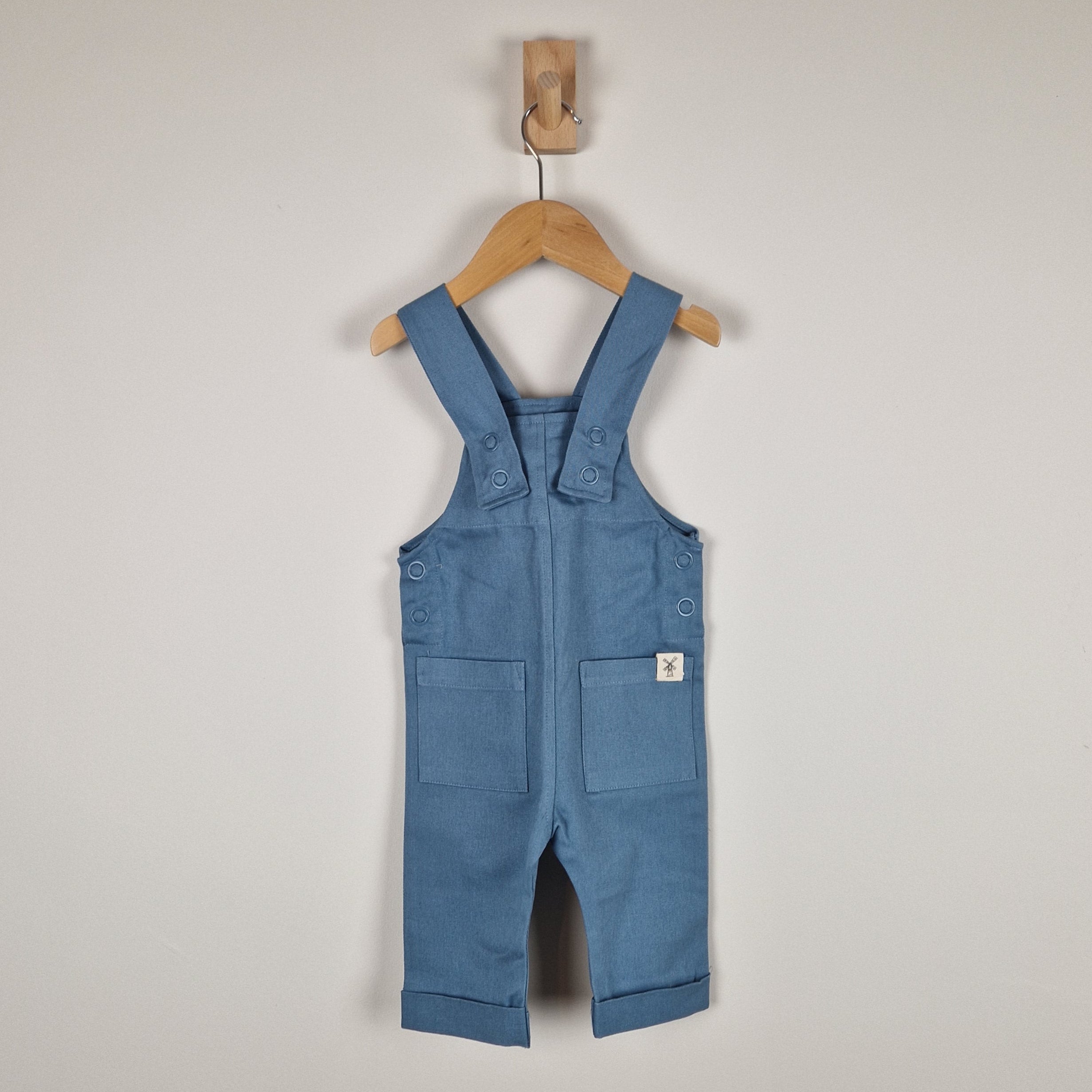 Blue denim overalls on a wooden hanger against a plain background