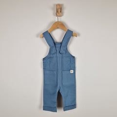 Blue denim overalls on a wooden hanger against a plain background