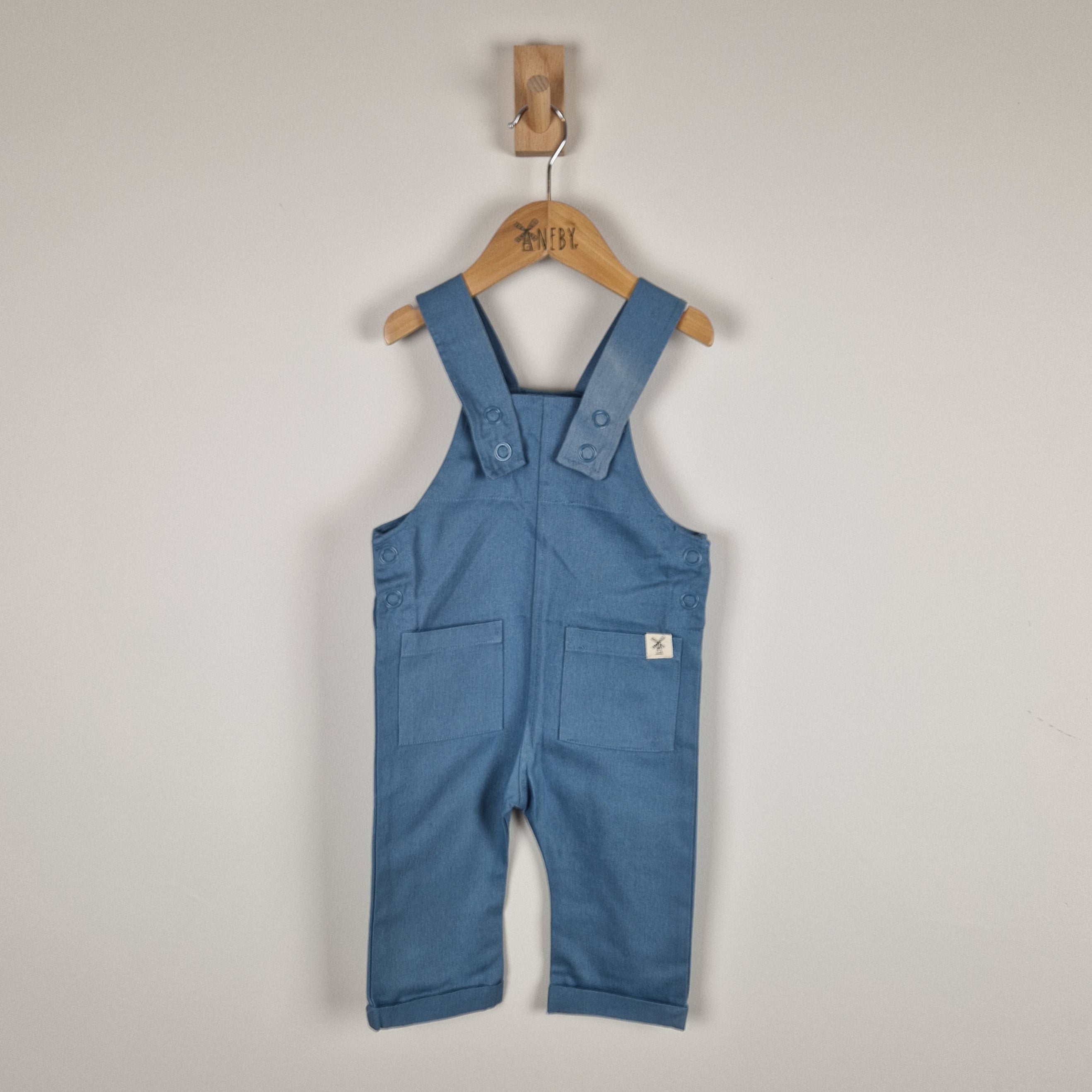 Blue children's overalls on a wooden hanger against a plain background