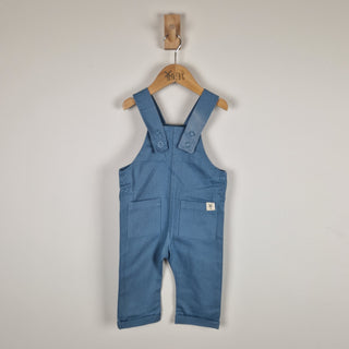 Blue children's overalls on a wooden hanger against a plain background