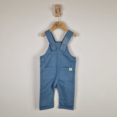Blue children's overalls on a wooden hanger against a plain background
