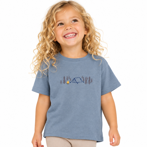 A young girl with curly blonde hair smiling while wearing a gre/blue short-sleeve t-shirt with a camping graphic on the chest, set against a plain white background.