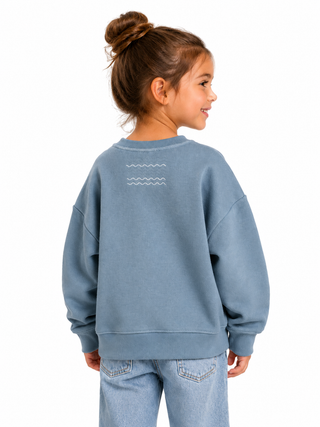 Child wearing a blue sweatshirt with a wave design on the back, standing against a white background.