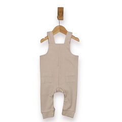 A baby's ribbed knit overall romper in a light beige color, hanging from a wooden hanger on a white background.