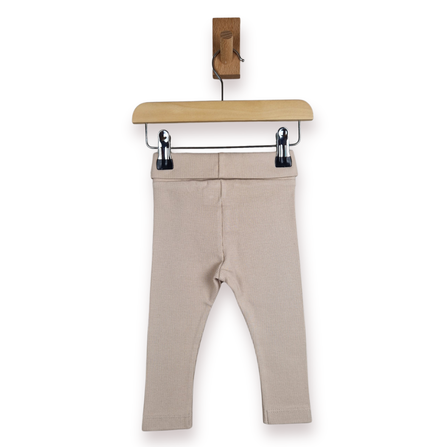 A pair of beige baby leggings hanging from a wooden hanger with black clips against a plain white background.
