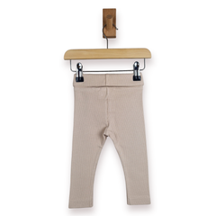 A pair of beige baby leggings hanging from a wooden hanger with black clips against a plain white background.