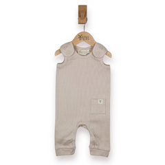 A baby sleeveless romper in a light taupe-beige colour, with shoulder straps and small pocket, hanging on a wooden hanger, against a plain white background.