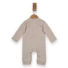 A light beige long-sleeve baby romper hanging on a wooden hanger from a wall hook, shown from the back against a plain white background.