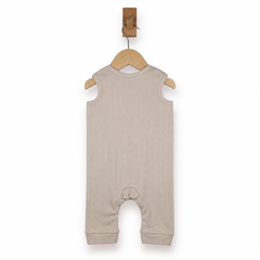 A sleeveless baby romper in a light oatmeal beige color, hanging on a wooden hanger from a wall hook against a plain white background.