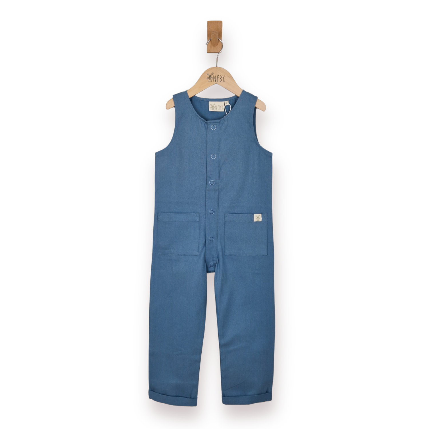 A sleeveless blue one-piece jumpsuit for toddlers, hanging on a wooden hanger with a wooden hook. The jumpsuit features a button-up front, two front patch pockets, and a small square brand label on the right pocket.