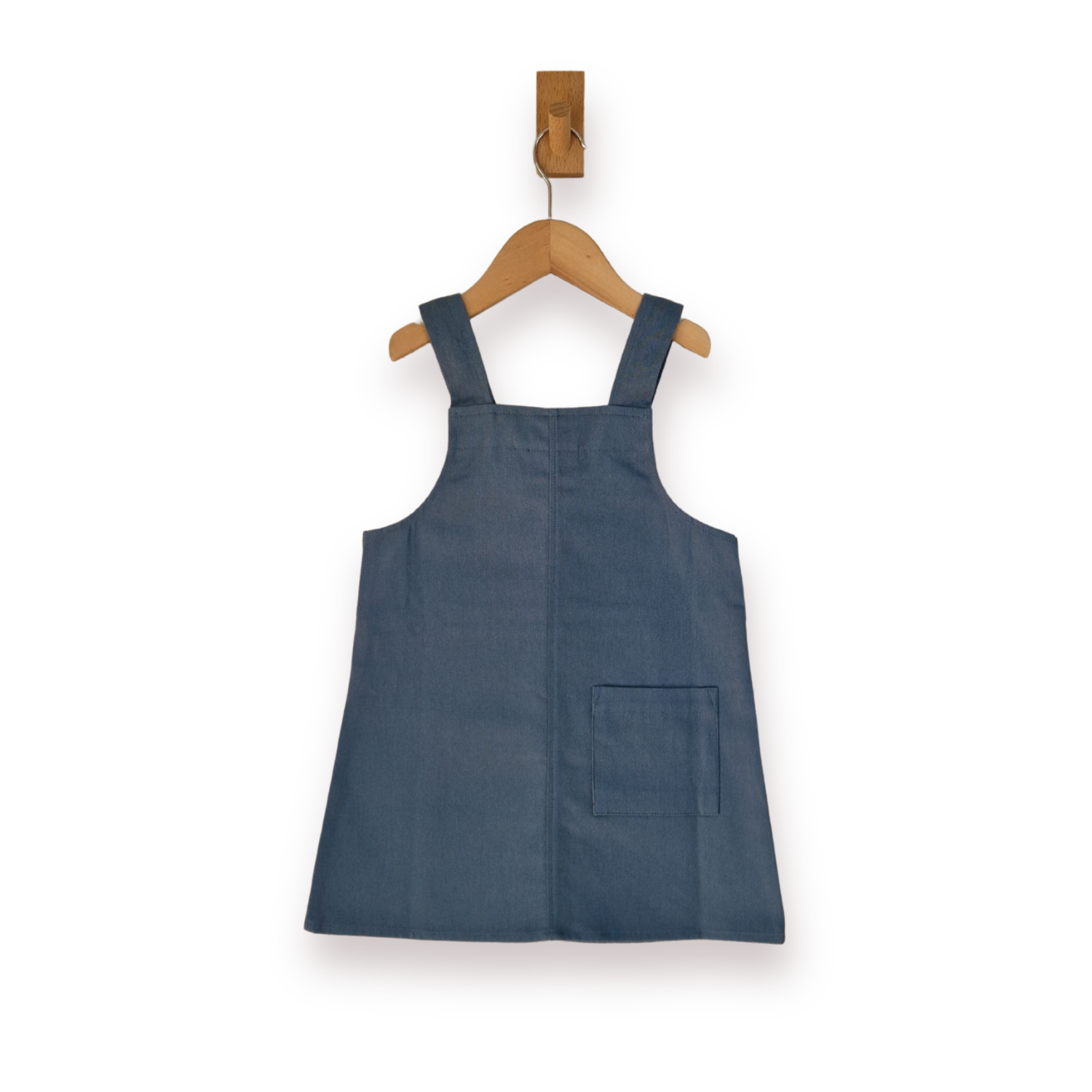 A slate blue sleeveless pinafore-style dress with shoulder straps and a front patch pocket, hanging on a wooden hanger against a plain white background.