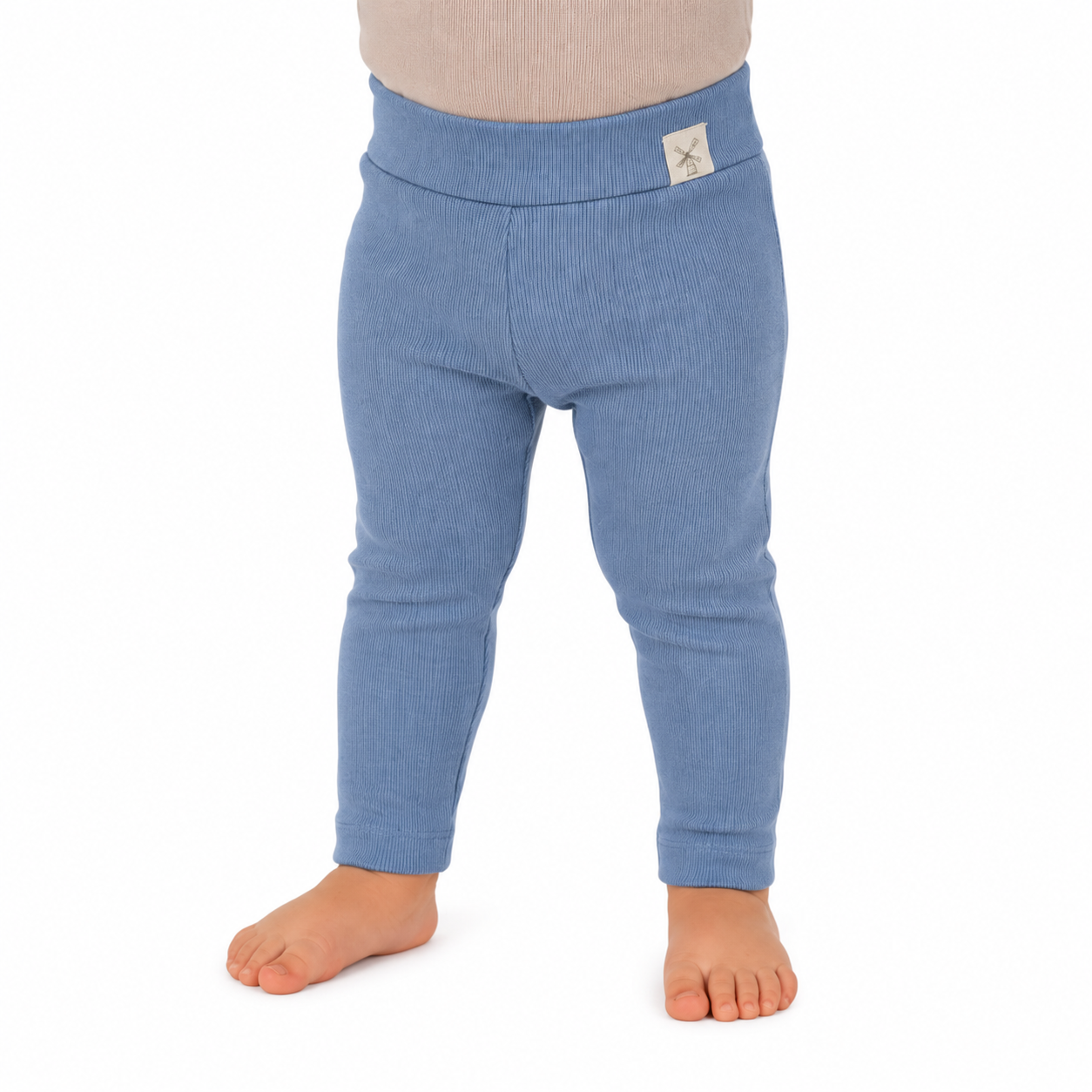 A child wearing ribbed blue leggings with a small white brand patch on the back waistband, standing barefoot against a white background.