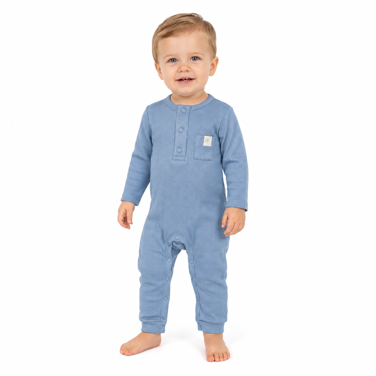 A toddler standing against a plain white background wearing a light blue long-sleeve footless one-piece romper with a buttoned neckline and a small brand patch on the chest pocket.