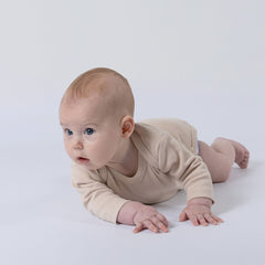 Small baby laying on the floor, wearing long-sleeved body suit in gender-neutral oat