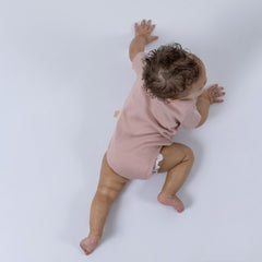 Baby trying to crawl wearing pink short sleeve bodysuit with Aneby windmill hem tag in side seam 