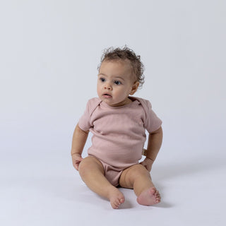 Baby wearing short sleeve jersey rib bodysuit in soft pink with envelope neckline and crotch poppers
