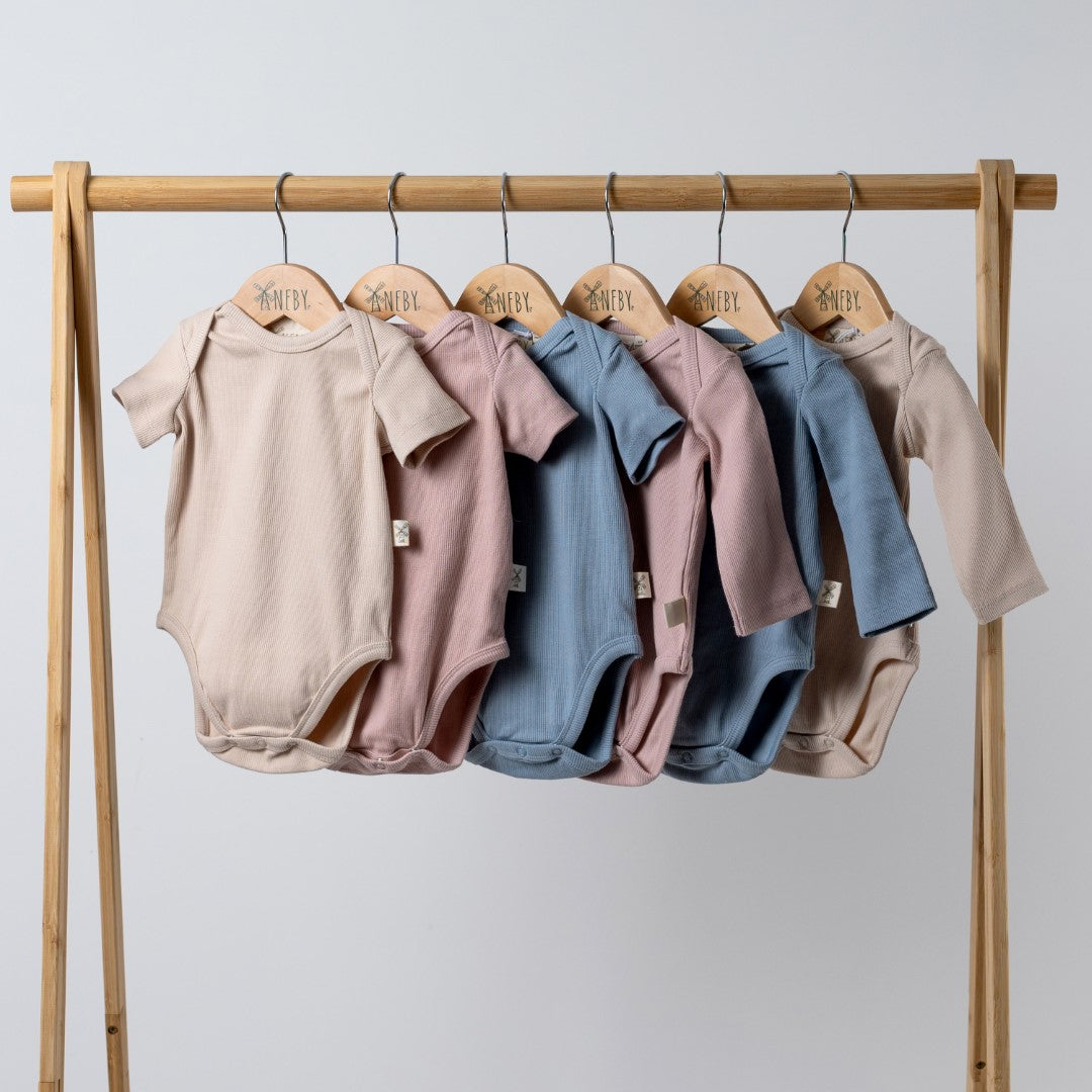 6 short sleeve and long sleeve baby bodysuits in oat, pink and blue on wooden clothes rail