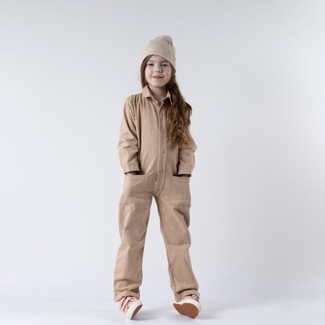 Young girl wearing beige boilersuit with both hands in the front patch pockets