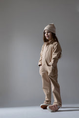 Girl wearing neutral oat cotton twill jumpsuit with beanie hat