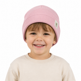A smiling young child wearing a light pink ribbed knit beanie with a small white embroidered logo patch on the side, photographed against a clean white background.