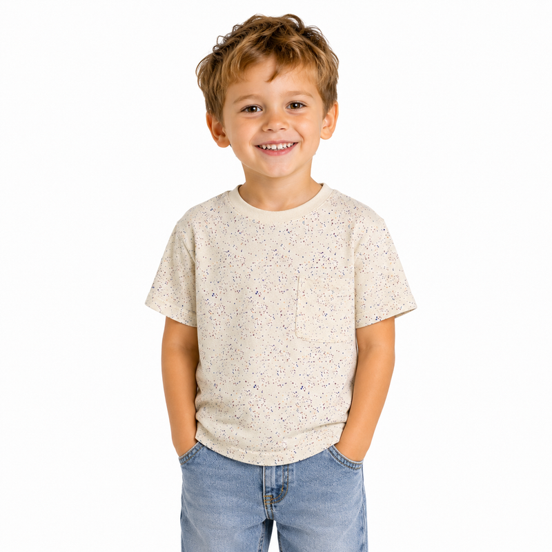 Boy wearing an ecru t shirt with paint flecks all over, smiling at the camera. On a blank white background.