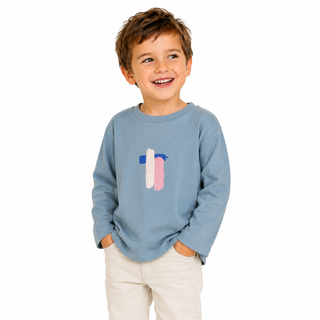 Boy wearing a long sleeve blue tshirt with a fun arty print in blue, beige and pink. He is smiling, looking to the side on a white background. 