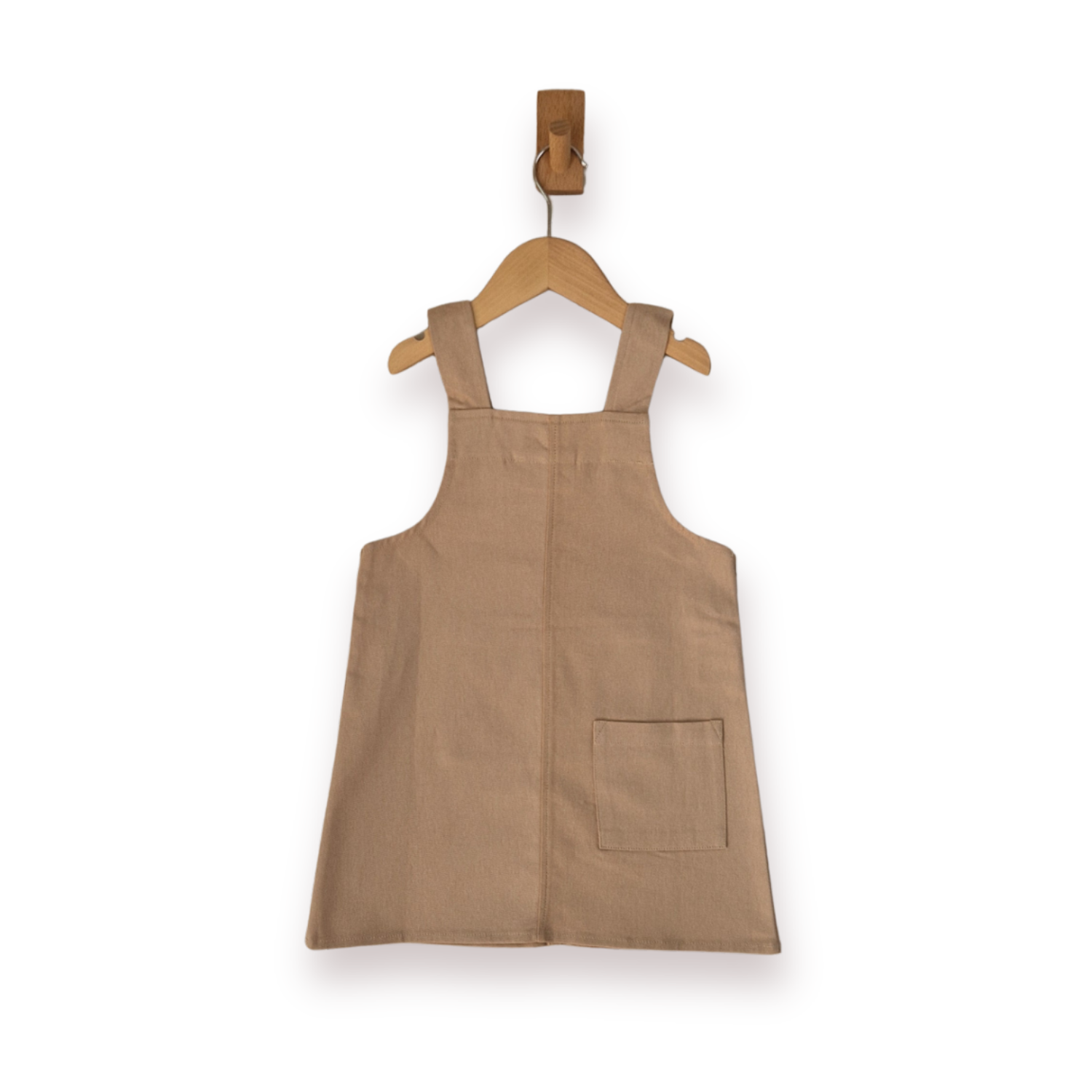 A sleeveless ecru pinafore-style dress with shoulder straps and a front patch pocket, hanging on a wooden hanger against a plain white background.
