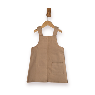 A sleeveless ecru pinafore-style dress with shoulder straps and a front patch pocket, hanging on a wooden hanger against a plain white background.