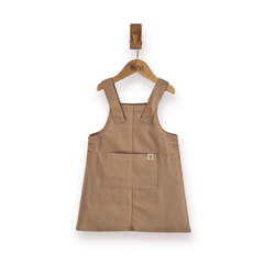 A sleeveless ecru utility pinafore style dress with a front patch pocket, hanging on a wooden hanger, set against a plain white background.