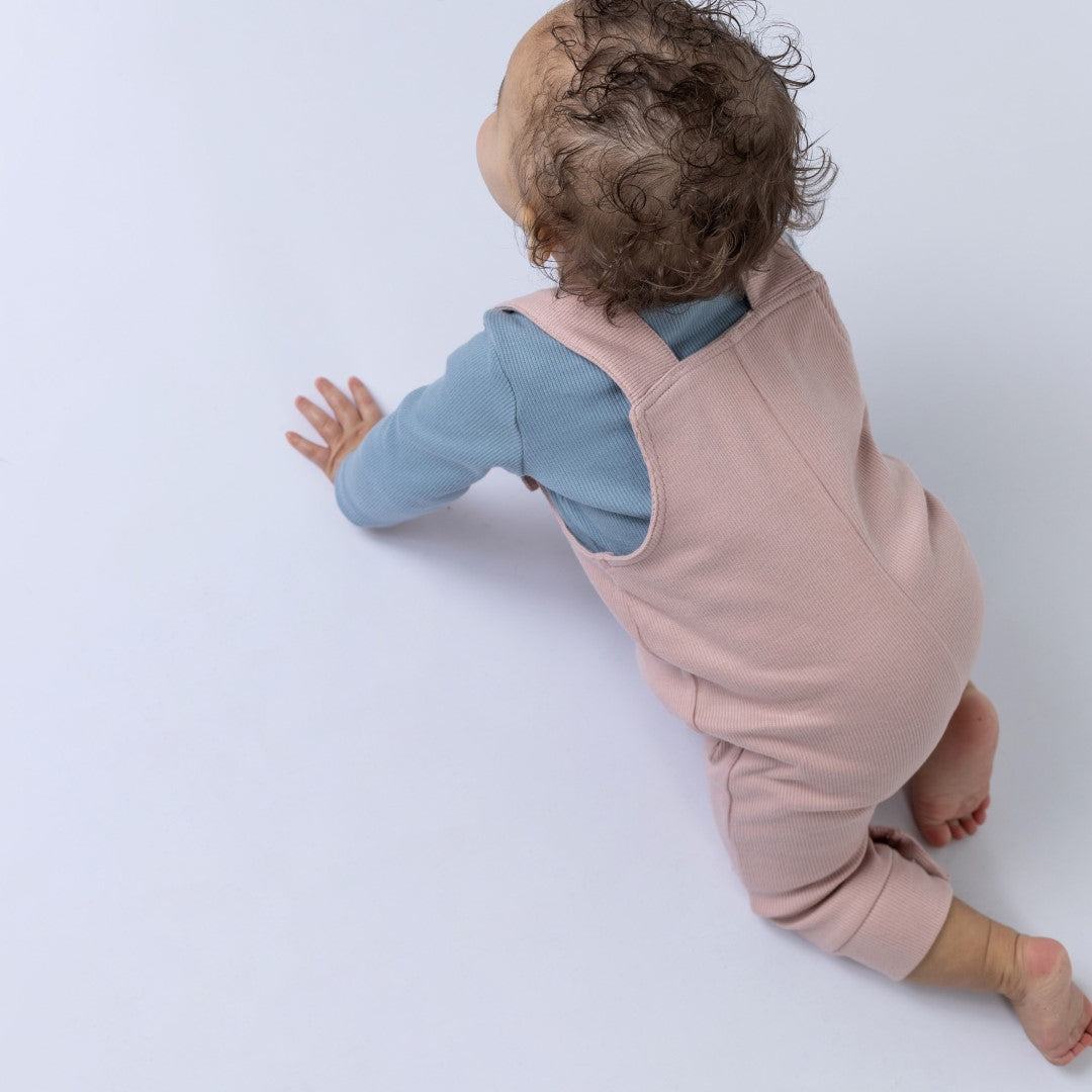Small baby girl attempting to crawl whilst wearing gender-neutral pink dungarees