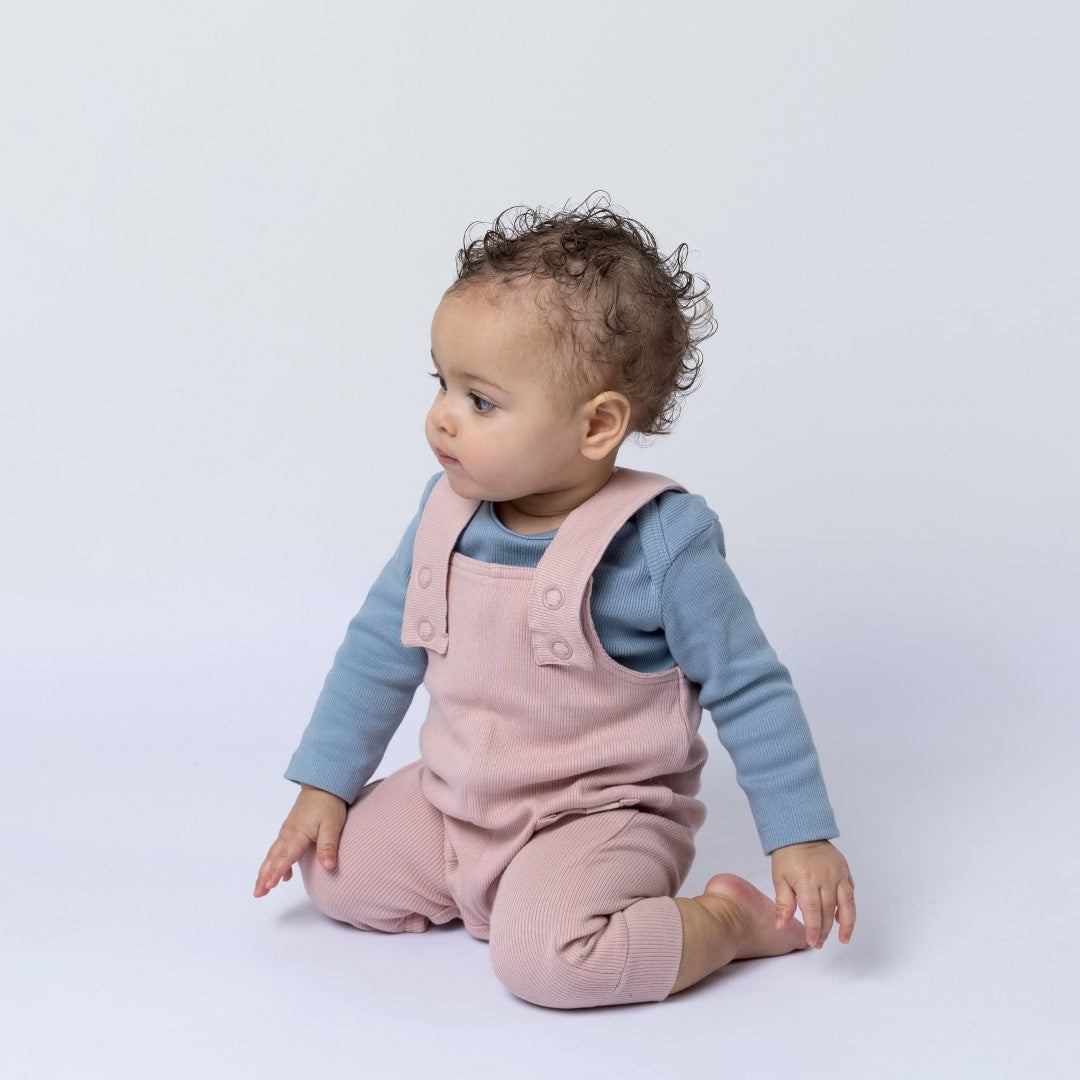 Small baby wearing pink dungarees with a blue romper