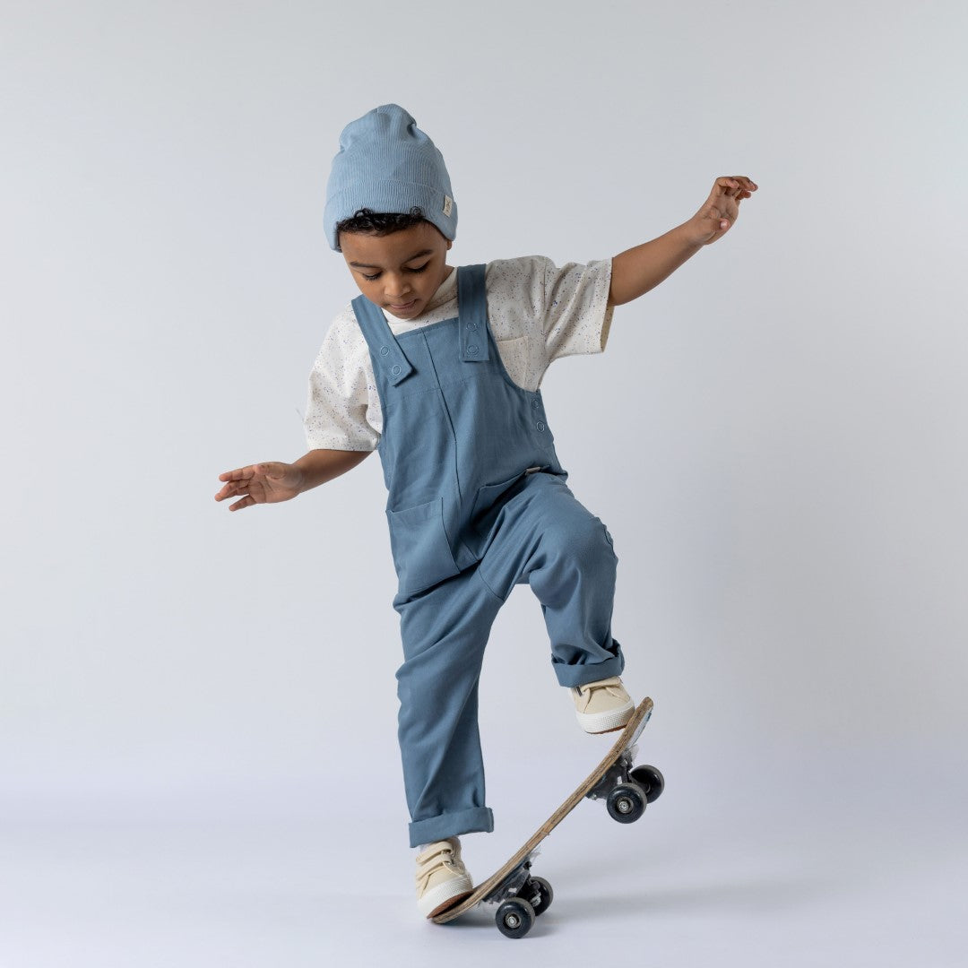 Blue dungarees with rolled hem and dyed to match poppers being modelled by young boy on skateboard