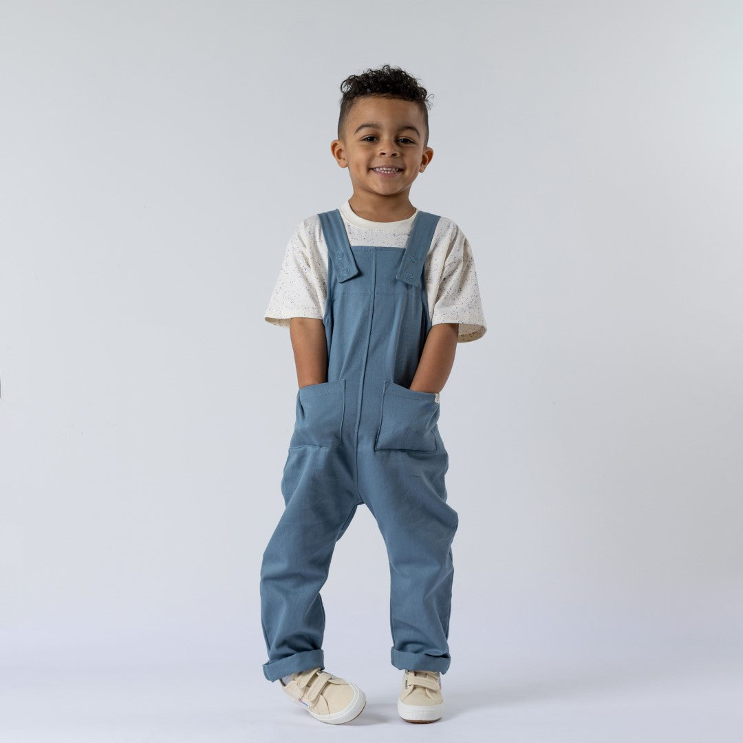 Blue dungarees with front pockets and shoulder straps being modelled by young boy