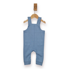 A baby's blue rib cotton overall romper hanging from a wooden hanger on a wall hook, against a plain white background.