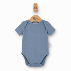 A baby short-sleeve bodysuit in dusty blue, hanging on a wooden hanger from a wooden peg against a clean white background.