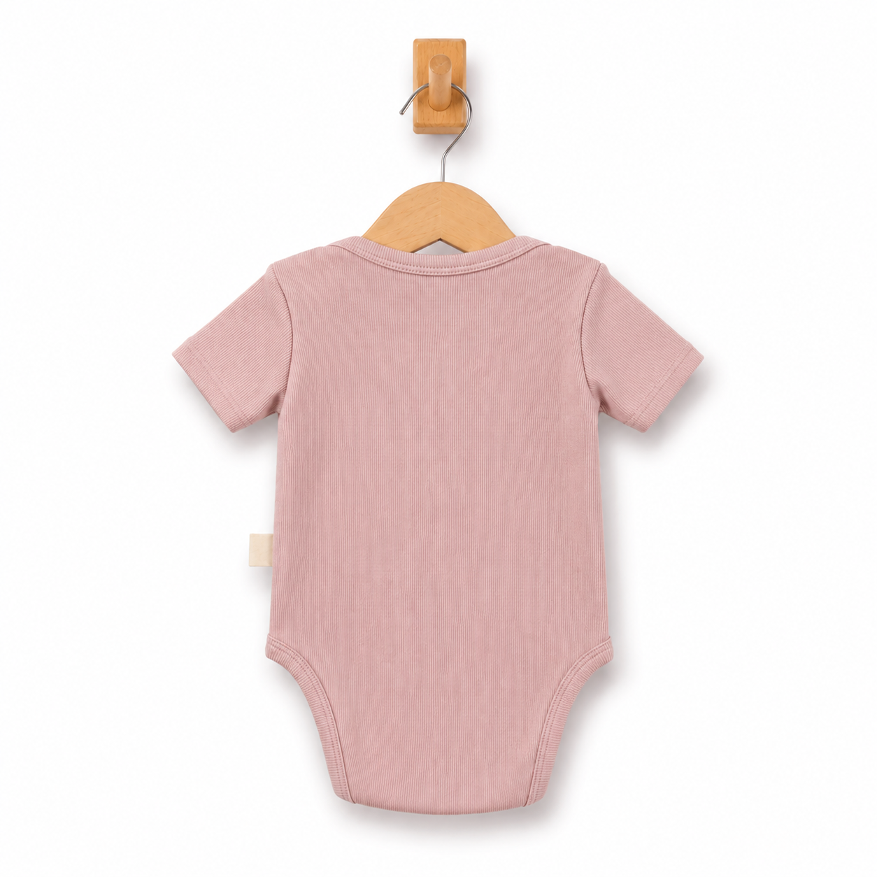 A dusty pink short-sleeve baby bodysuit shown from the back, hanging on a wooden hanger from a wall hook against a clean white background.