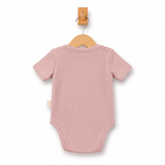 A dusty pink short-sleeve baby bodysuit shown from the back, hanging on a wooden hanger from a wall hook against a clean white background.