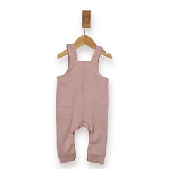 A dusty pink baby dungarees with shoulder straps, hanging from a wooden hanger on a white background.