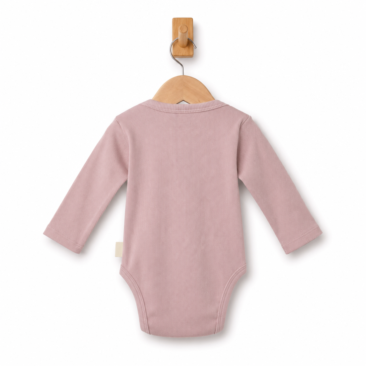A dusty pink long-sleeve baby bodysuit shown from the back, hanging on a wooden hanger from a wall hook against a clean white background.