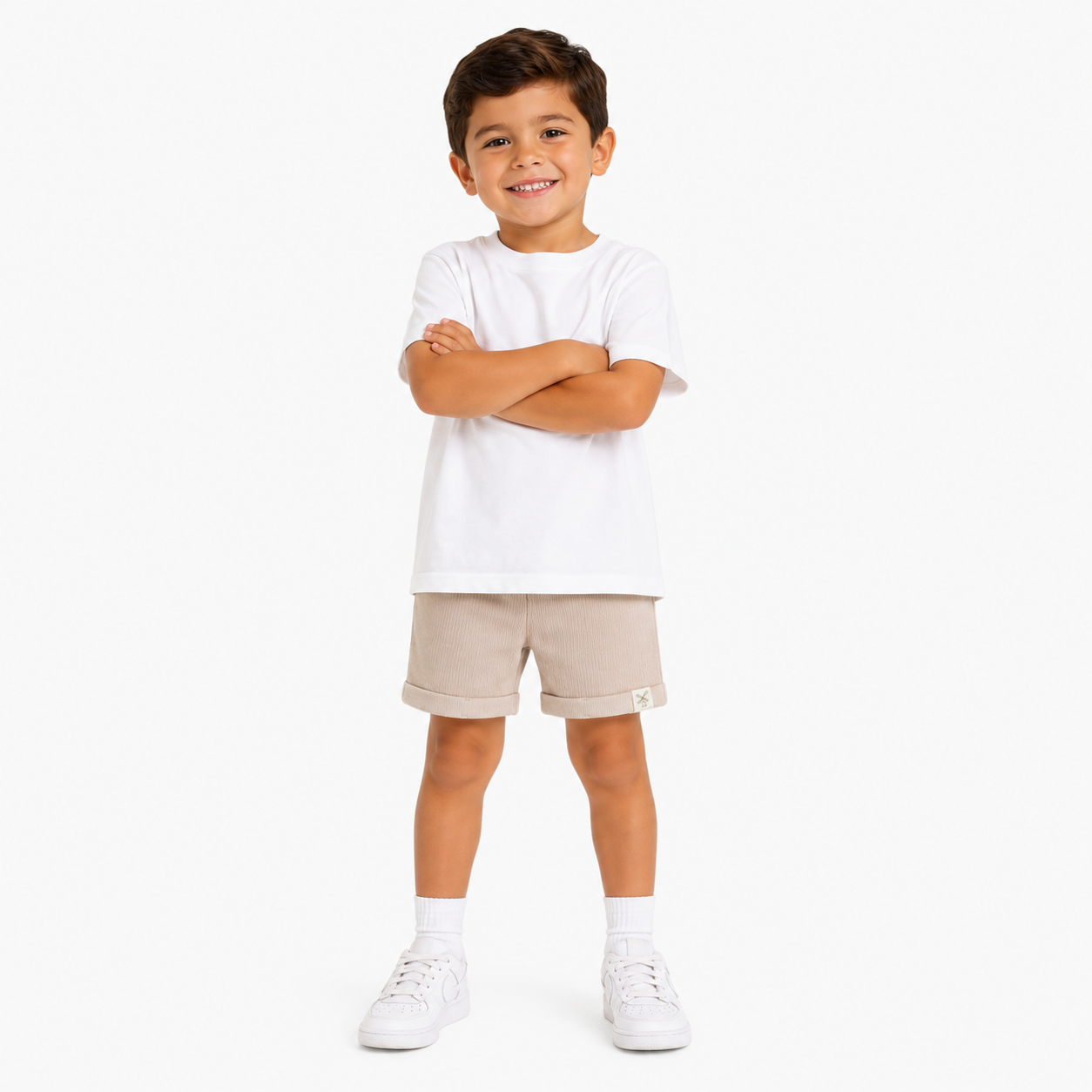 A young boy modeling a white short-sleeve crewneck t-shirt and beige rolled-calf shorts, paired with white socks and trainers, standing against a white studio background.