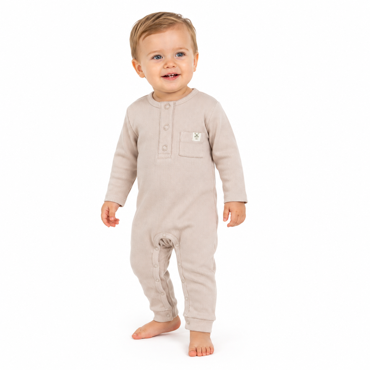 A baby wearing a light beige long-sleeve footless romper with a three-button henley neckline and a chest pocket, standing against a plain white background.